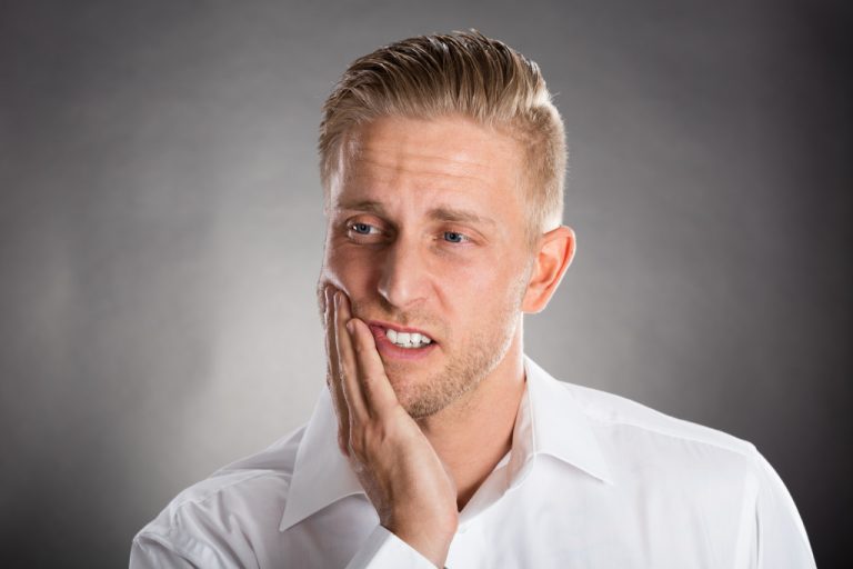 Young Man Suffering From Toothache Against Grey Background